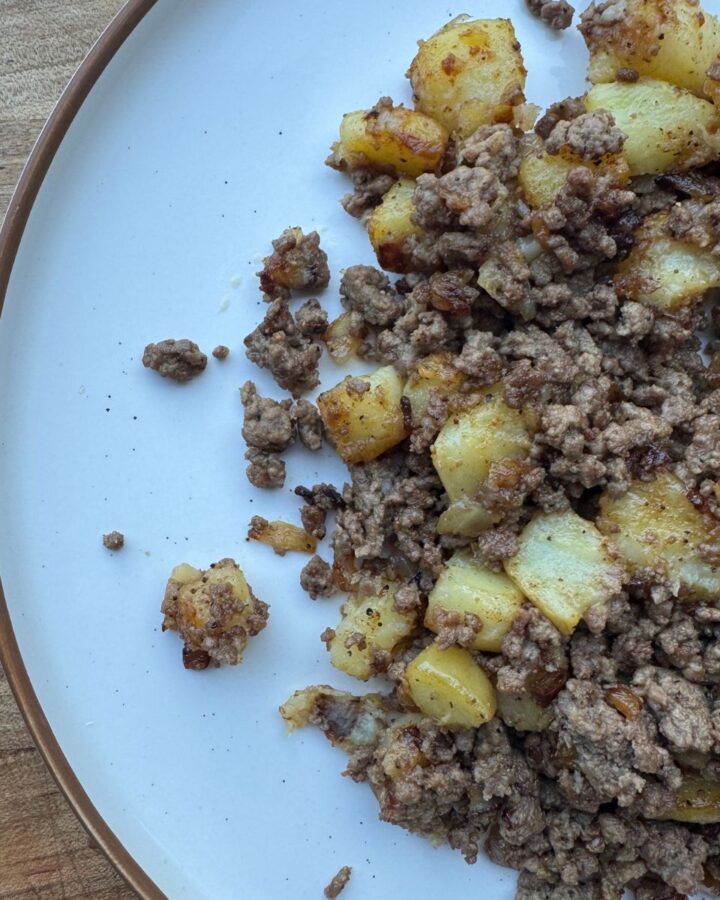 Ground beef and potatoes on white plate with wood background